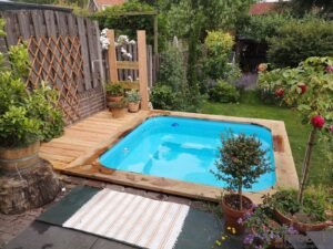 Bain nordique au bois TimberIN Nordic Square, avec un écran d’intimité, entouré de plantations de jardin, sur une terrasse en bois, dans un jardin paysager