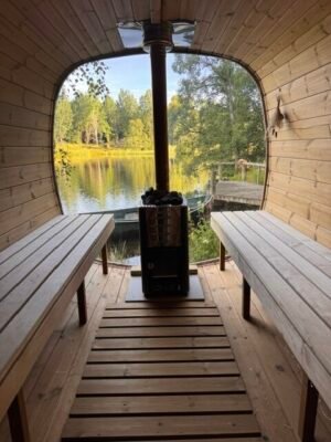 Intérieur du sauna mobile TimberIN Nordic Square avec bancs en bois et poêle à bois au bord d’un lac