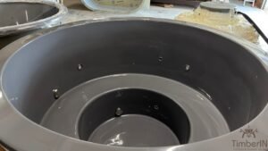 Vue intérieure d'un bain nordique vide en PRV gris avec plusieurs éclairages LED sous-marines rondes intégrées, jets et siège en forme
