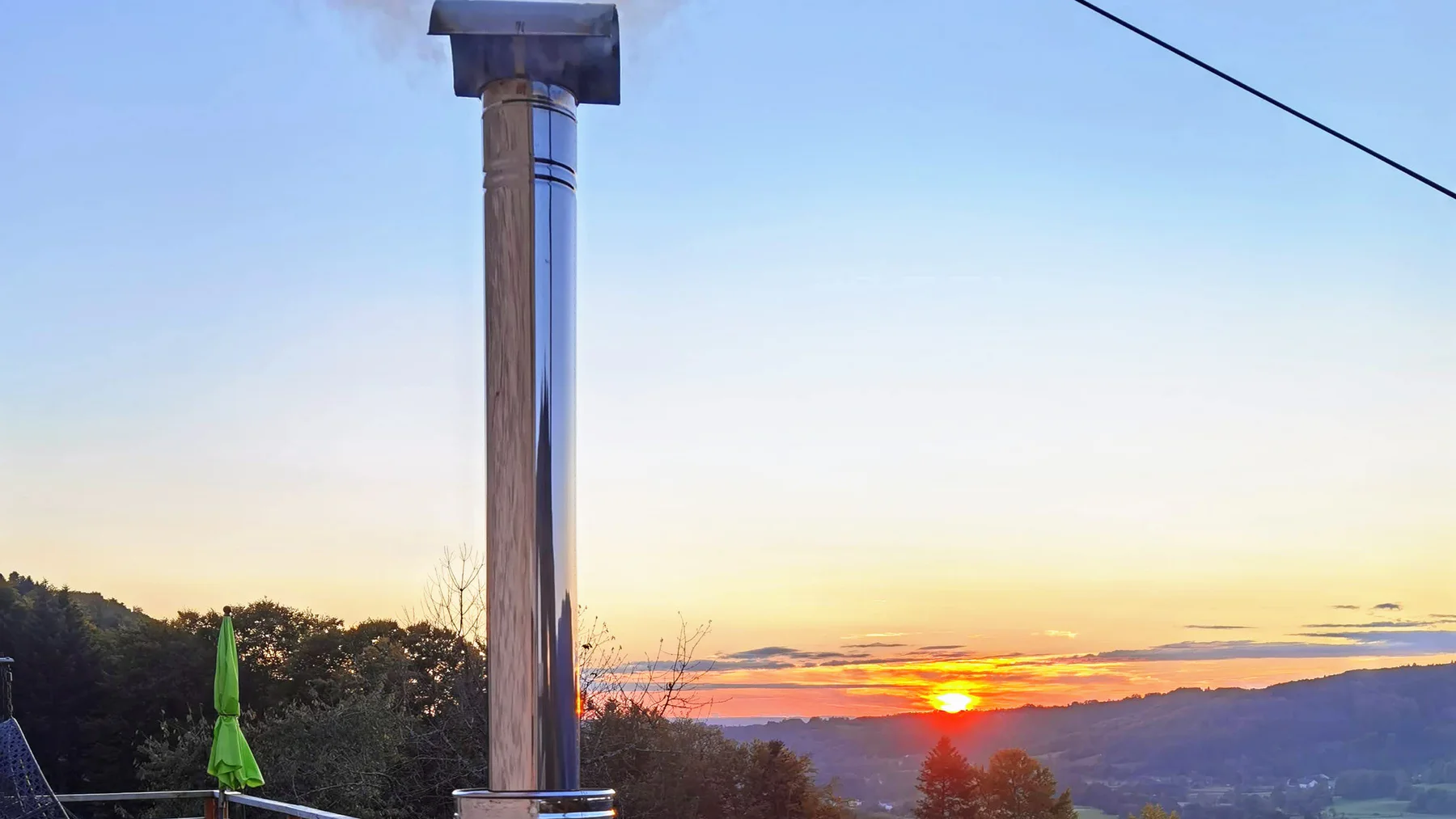 Conduit vertical d’un poêle extérieur TimberIN au coucher du soleil