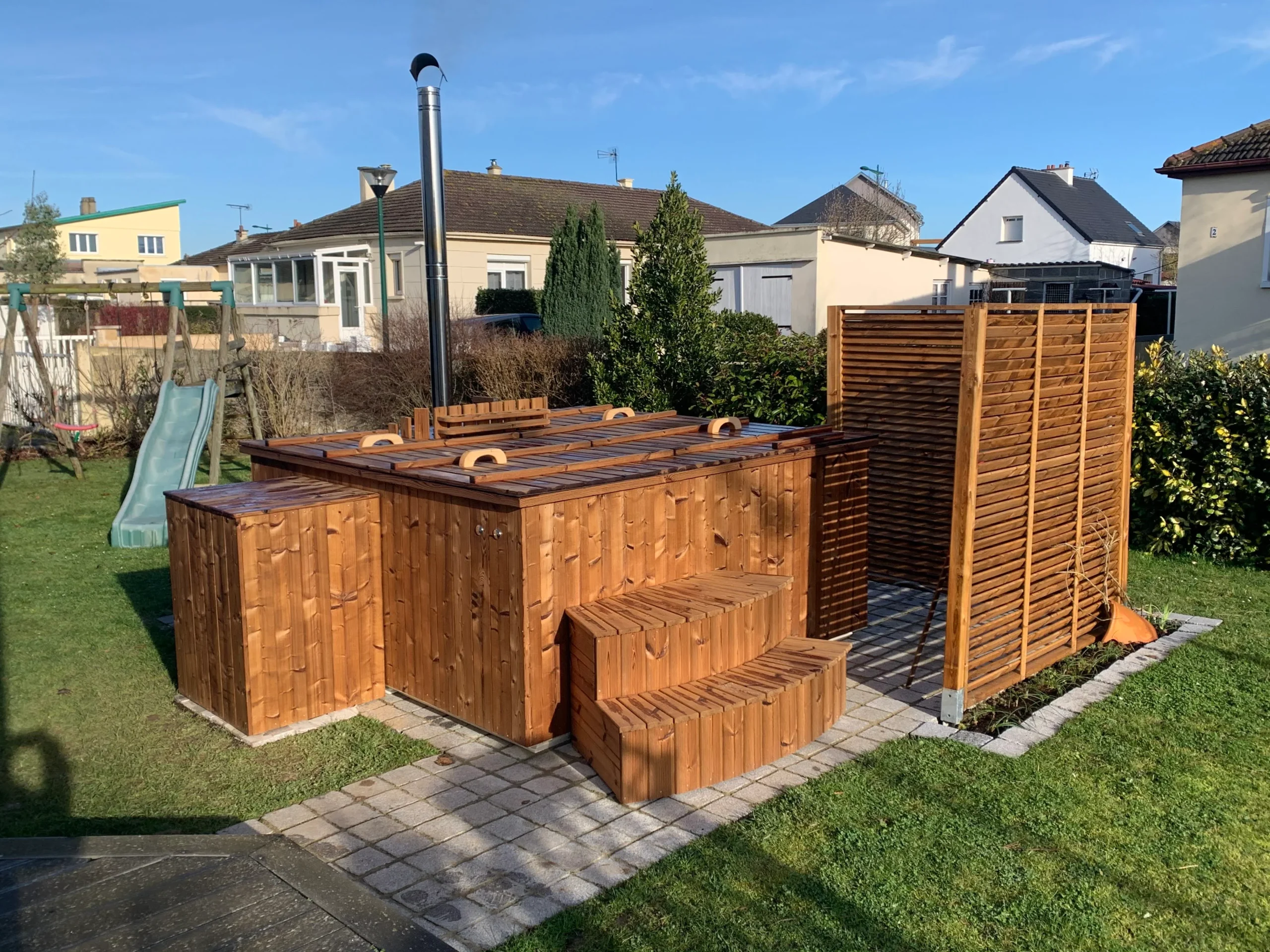 Pourquoi choisir TimberIN ? 6 Bain nordique carré en bois avec couvercle, marches et claustra installé dans un jardin résidentiel