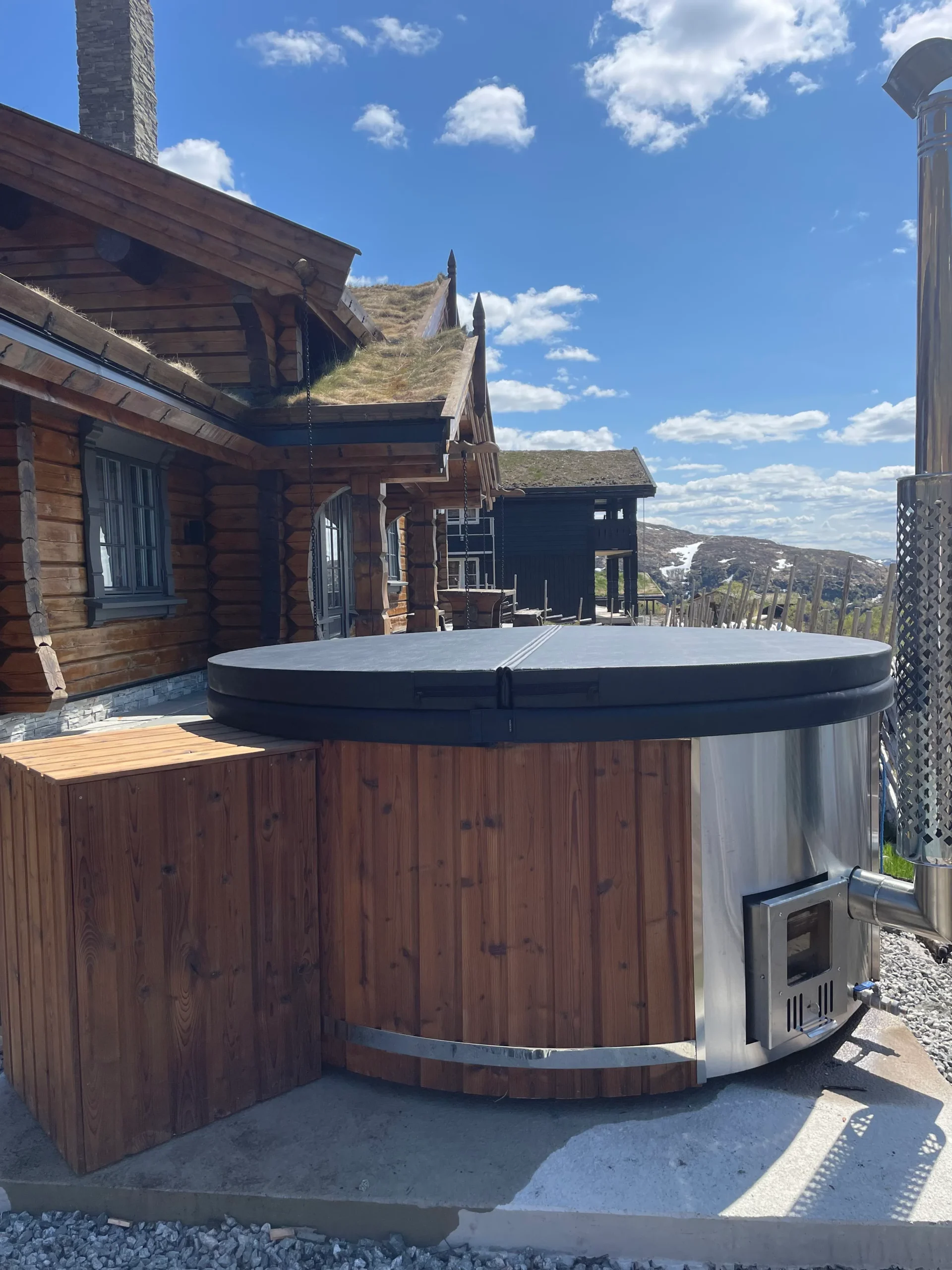 Pourquoi choisir TimberIN ? 8 Bain nordique en bois avec poêle extérieur et couvercle installé près de chalets de montagne