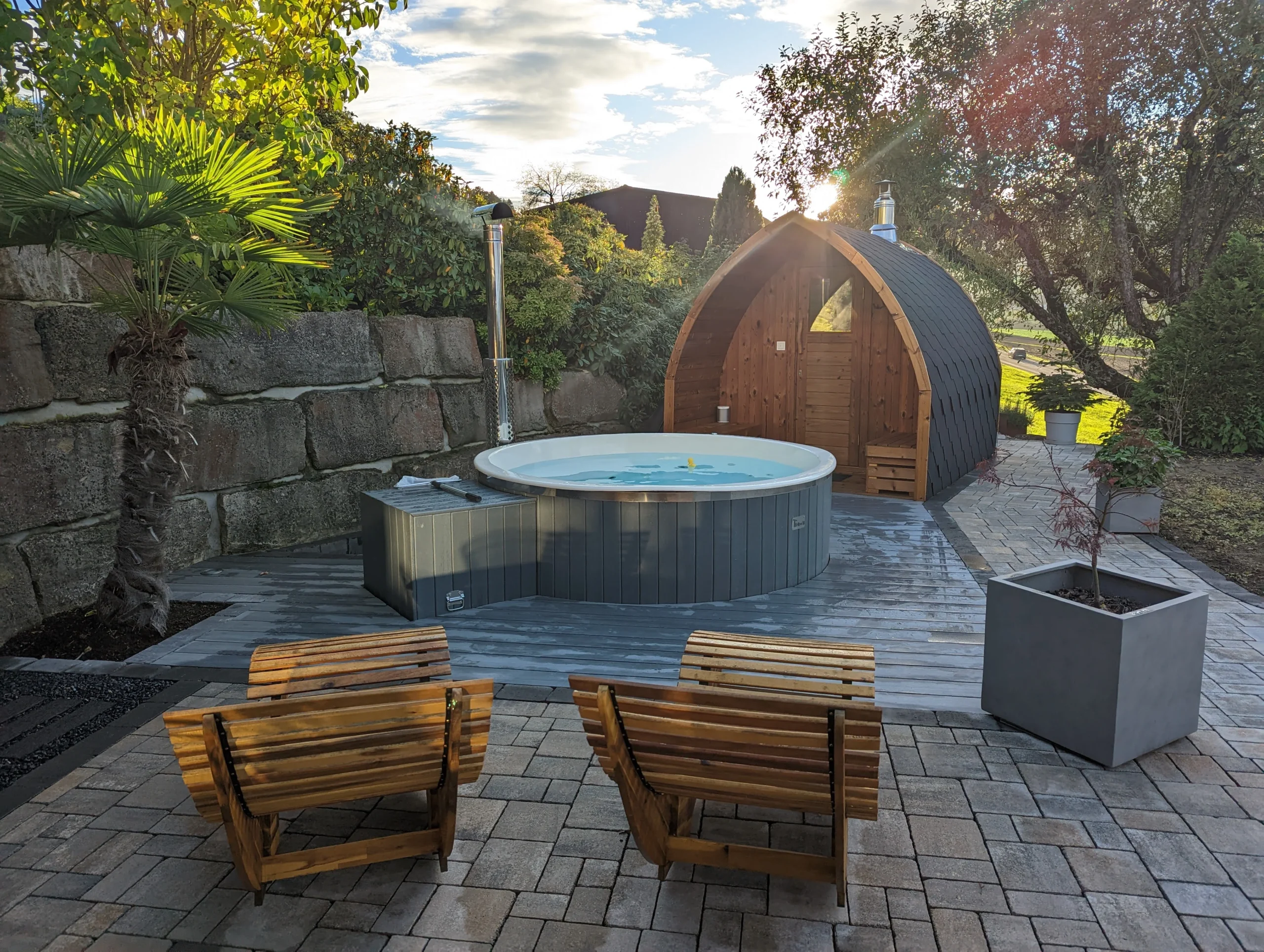 Pourquoi choisir TimberIN ? 4 Bain nordique gris et sauna pod en bois installés sur une terrasse paysagée avec assises extérieures